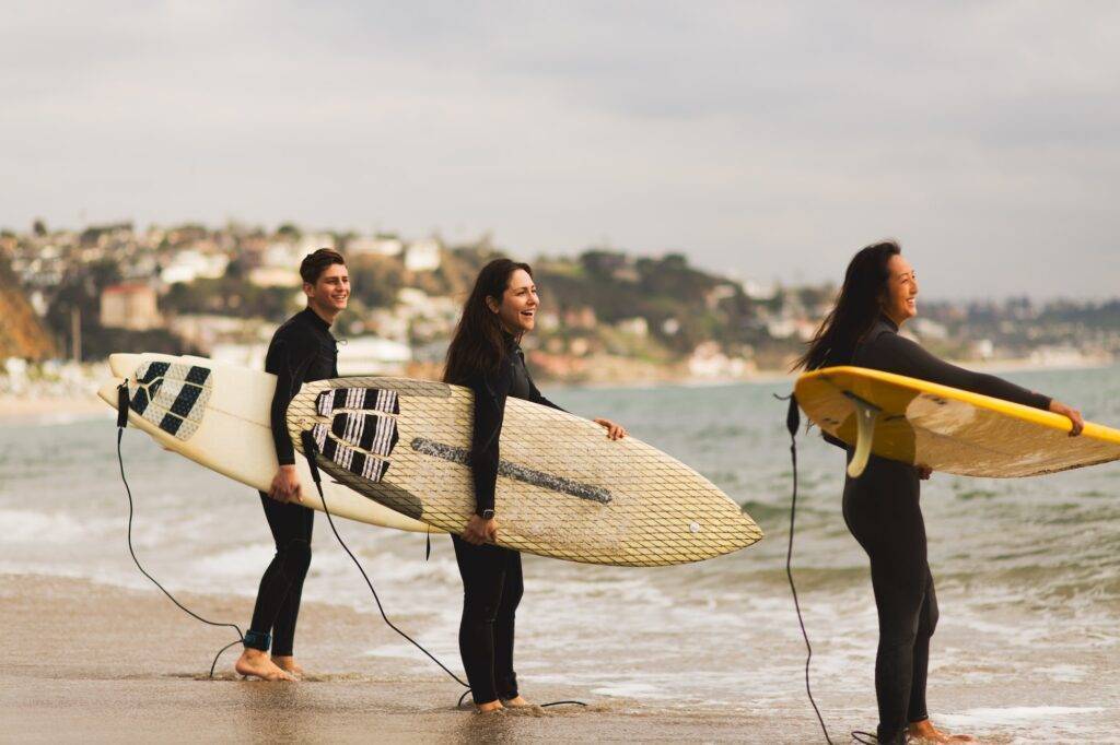 Three friends standing in sea, holding surfboards, preparing to surf