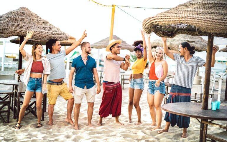 Beach Clubs en Marbella: Vive la Experiencia Costera de Lujo en la Costa del Sol. Jóvenes amigos de moda bailando y divirtiéndose en chiringuito beach club.