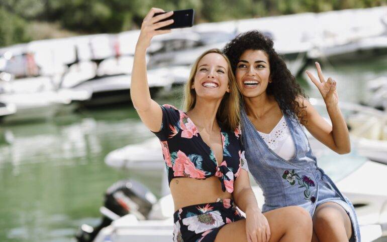 Marbella: A Glimpse for New Residents. Two happy young women taking a selfie at marina in summer