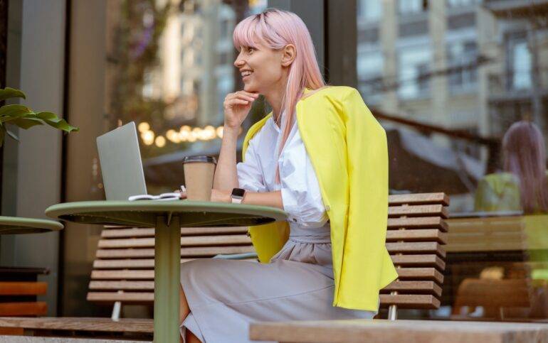 Joyful woman sitting at the table with laptop on the street